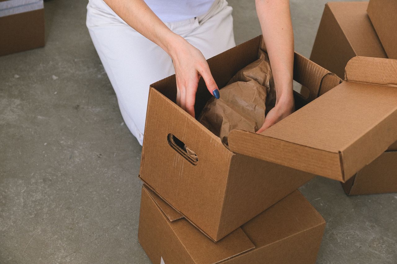 From above of crop anonymous relocating female packing wrapped items into carton box while preparing for moving to new apartment